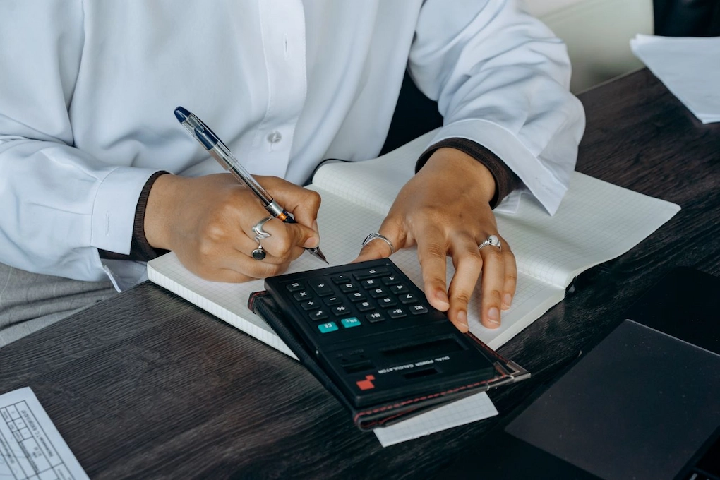 A man reviewing financial figures using a calculator and a notebook. Are grant funds taxable by KRA in Kenya?